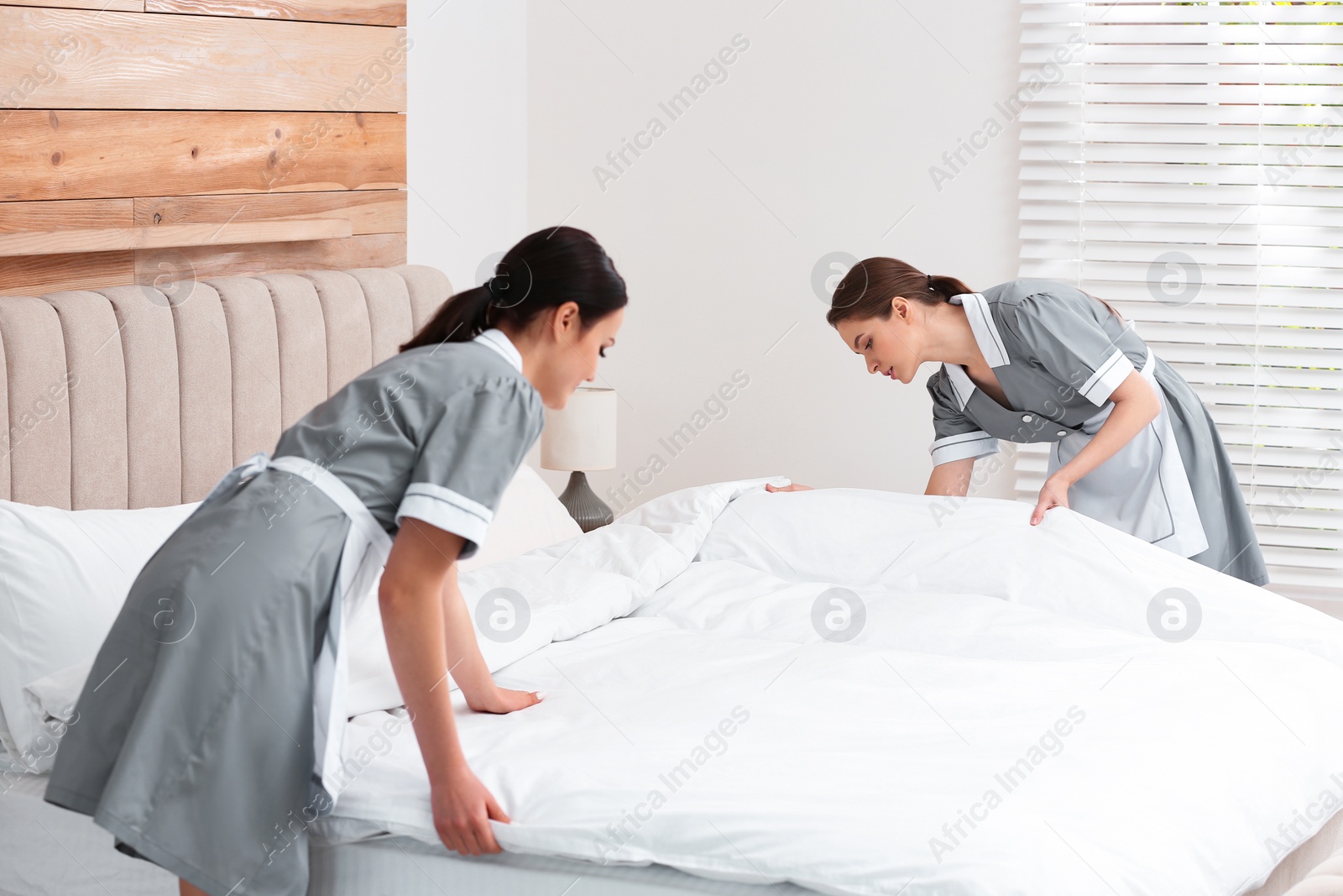 Photo of Young chambermaids making bed in hotel room