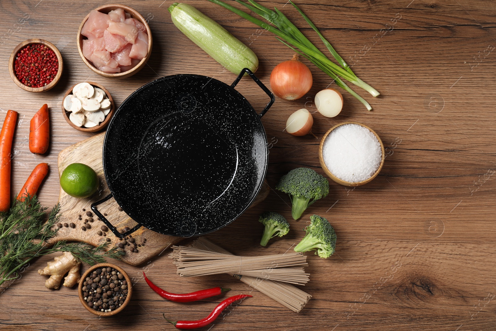 Photo of Empty iron wok surrounded by raw ingredients on wooden table, flat lay