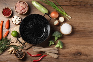 Photo of Empty iron wok surrounded by raw ingredients on wooden table, flat lay