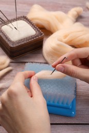 Photo of Woman felting from wool at wooden table, closeup