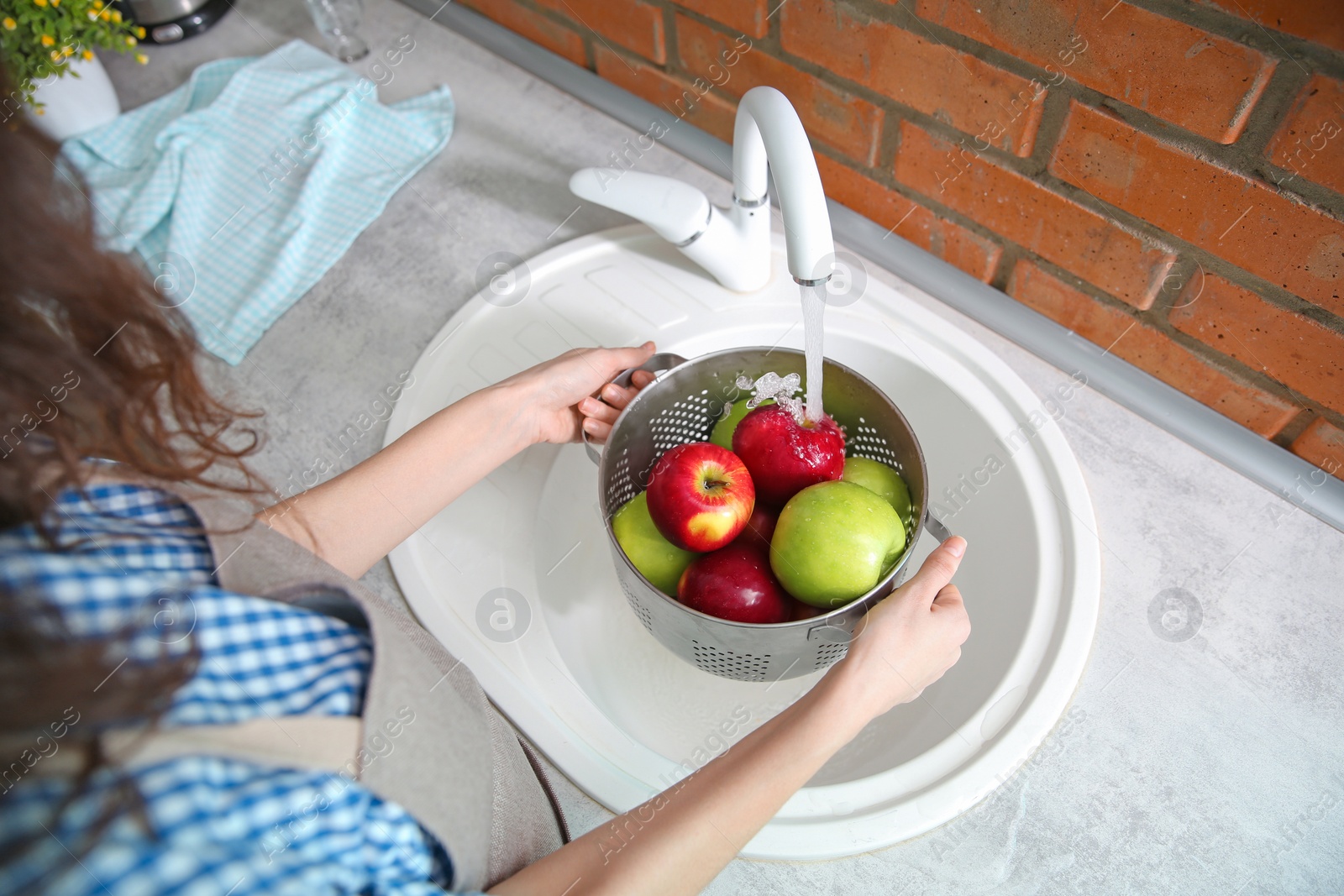 Photo of Young woman washing ripe apples in kitchen