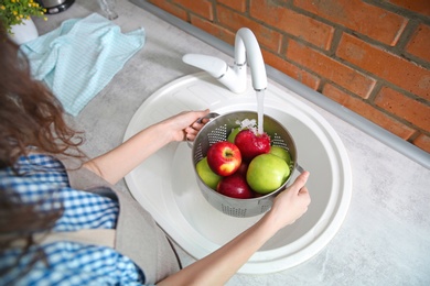 Young woman washing ripe apples in kitchen