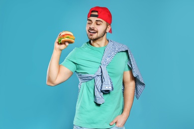 Photo of Handsome man with tasty burger on color background
