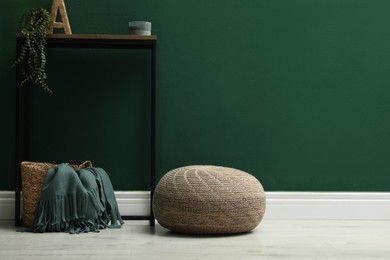 Stylish knitted pouf and table near green wall indoors, space for text
