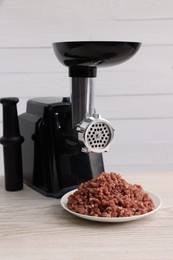 Electric meat grinder with beef mince on white wooden table