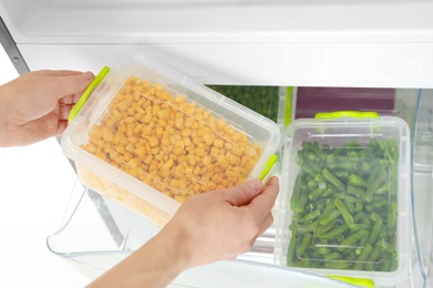 Photo of Woman taking container with frozen corn from refrigerator, closeup