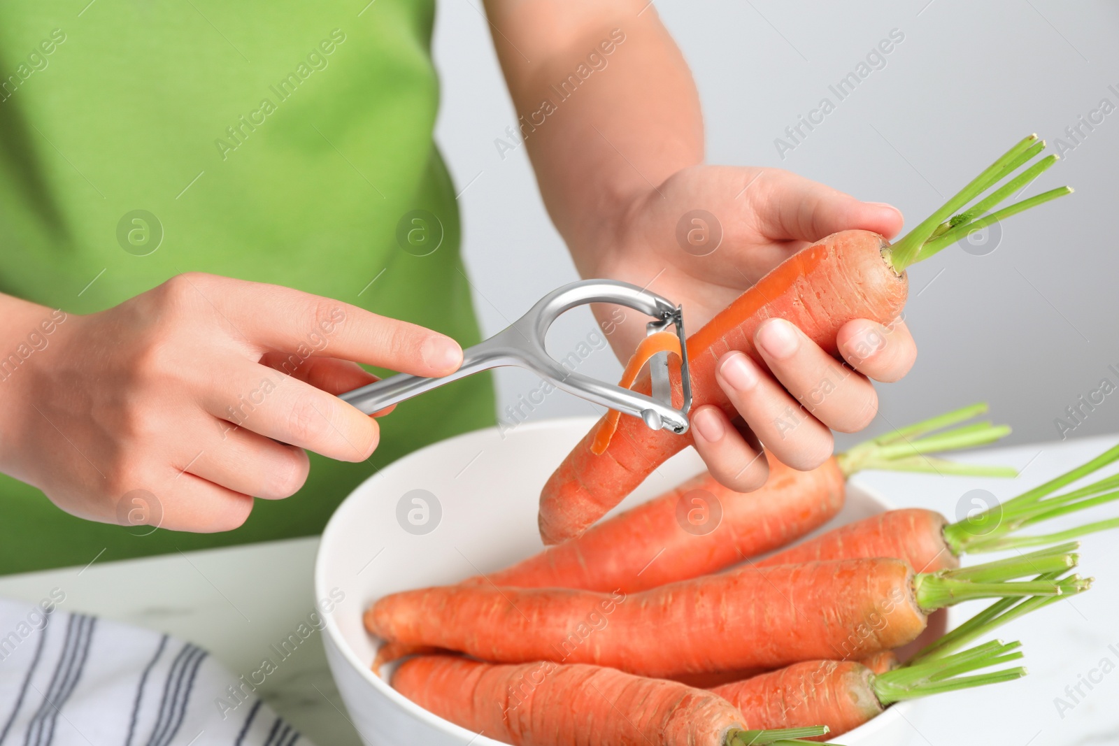 Photo of Woman peeling fresh carrot at white table indoors, closeup