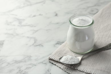 Baking powder in jar and spoon on white marble table, space for text