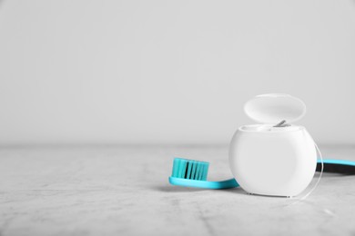 Container with dental floss and toothbrush on light grey textured table. Space for text