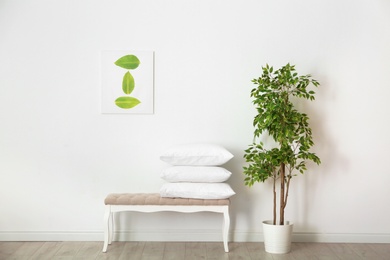 Photo of Pile of soft bed pillows on ottoman near wall in room