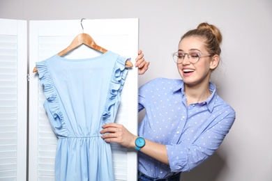 Young woman with clothes on hanger near folding screen against light background. Dressing room