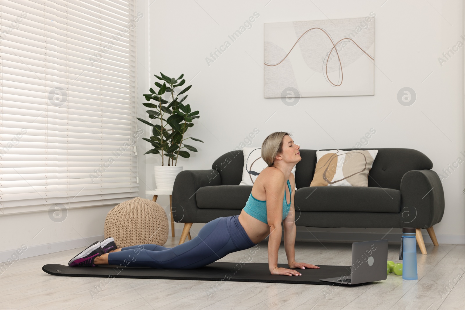 Photo of Online fitness trainer. Woman doing exercise near laptop at home