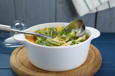 Saucepan of delicious vegetable soup with chicken and ladle on blue wooden table