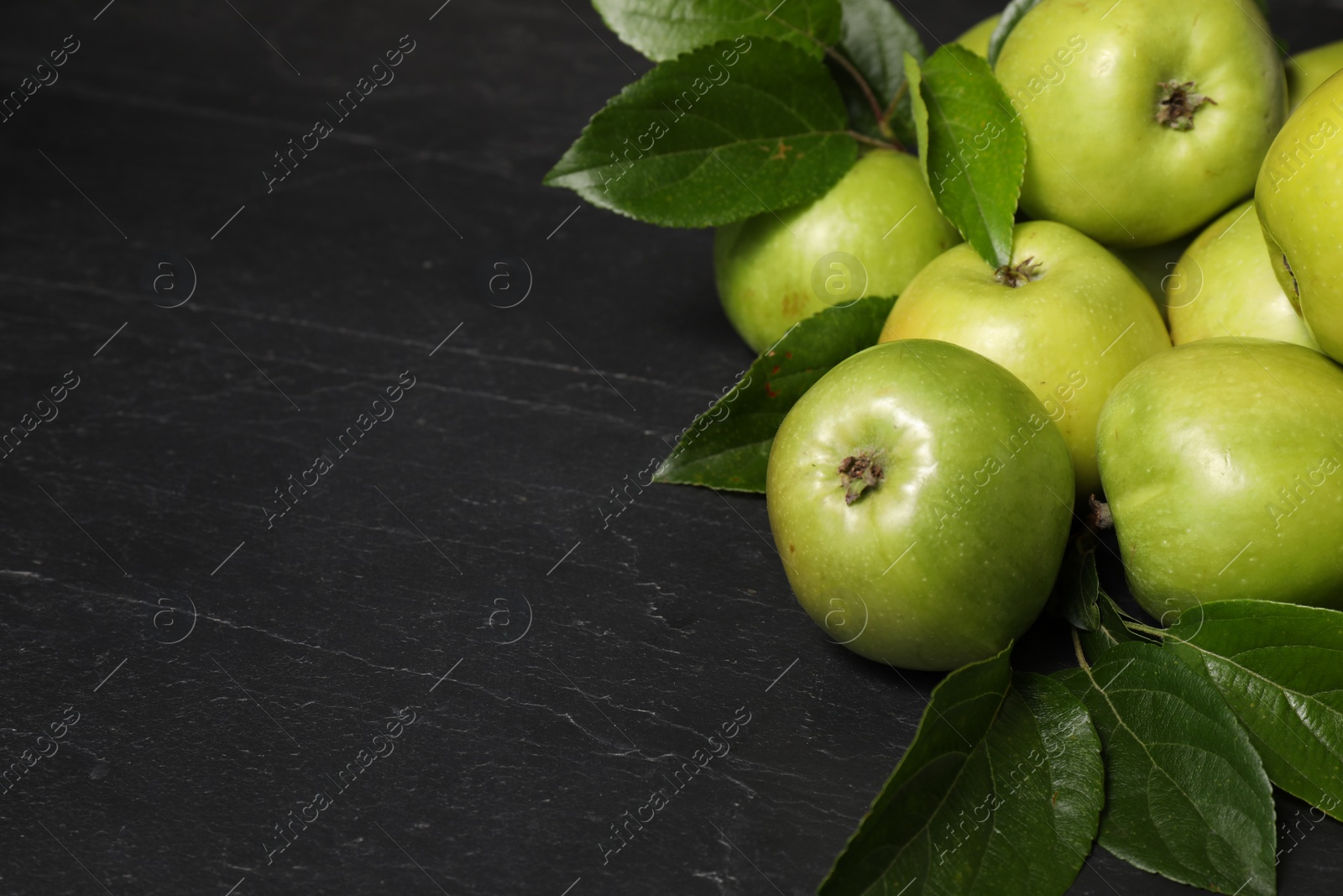 Photo of Ripe green apples with leaves on dark grey table, closeup