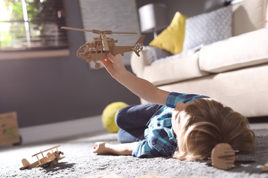 Photo of Little boy playing with cardboard helicopter on floor at home. Creative hobby