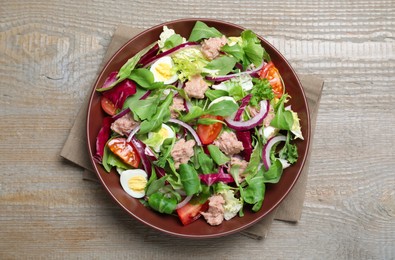 Photo of Bowl of delicious salad with canned tuna and vegetables on wooden table, top view