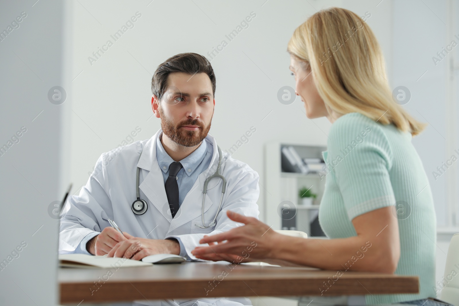 Photo of Doctor consulting patient at wooden table in clinic