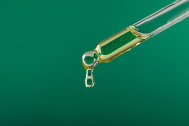 Dripping hydrophilic oil from pipette on green background, closeup. Space for text