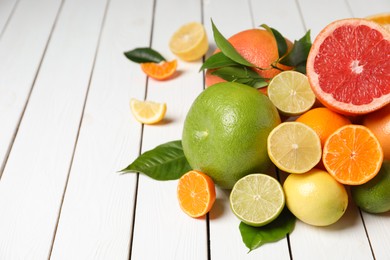 Photo of Different citrus fruits with fresh leaves on white wooden table. Space for text