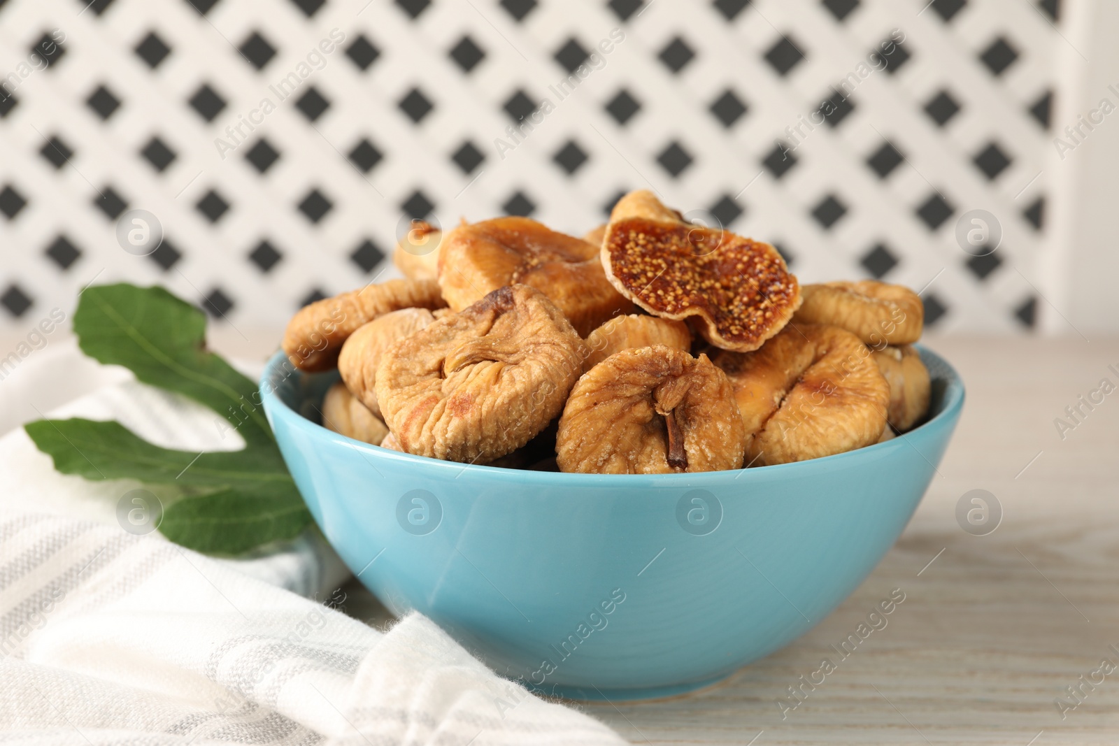 Photo of Bowl with tasty dried figs and green leaf on white wooden table, closeup