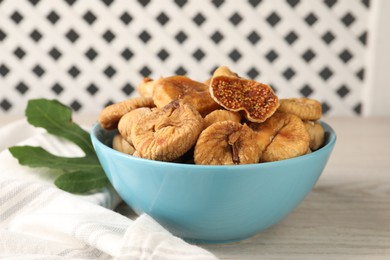 Bowl with tasty dried figs and green leaf on white wooden table, closeup