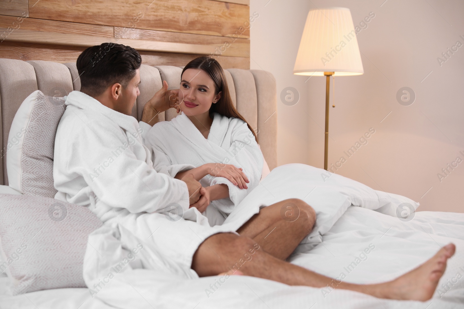 Photo of Happy couple in bathrobes resting on bed at home