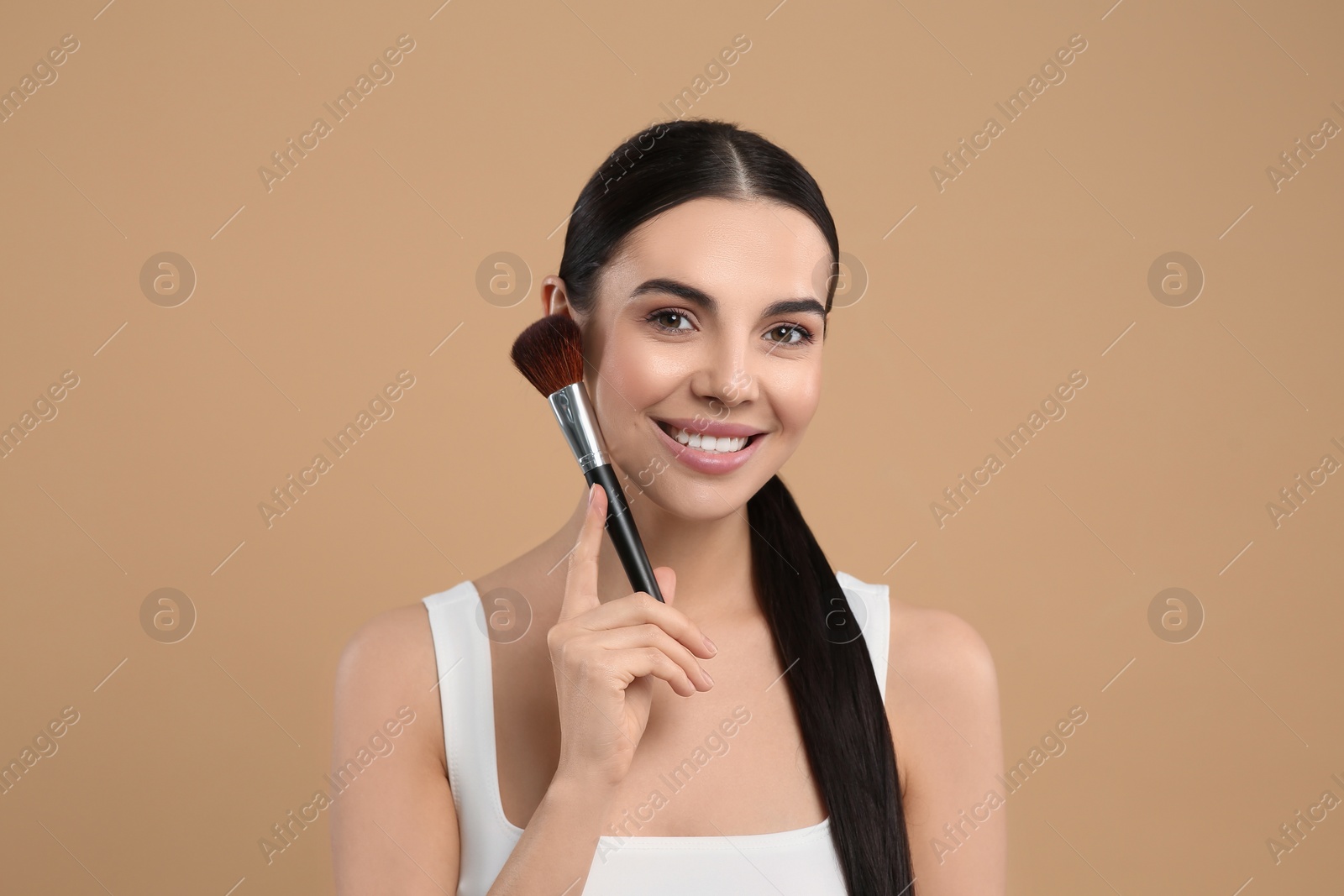 Photo of Beautiful woman with makeup brush on light brown background