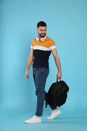 Young man with stylish backpack and headphones on light blue background