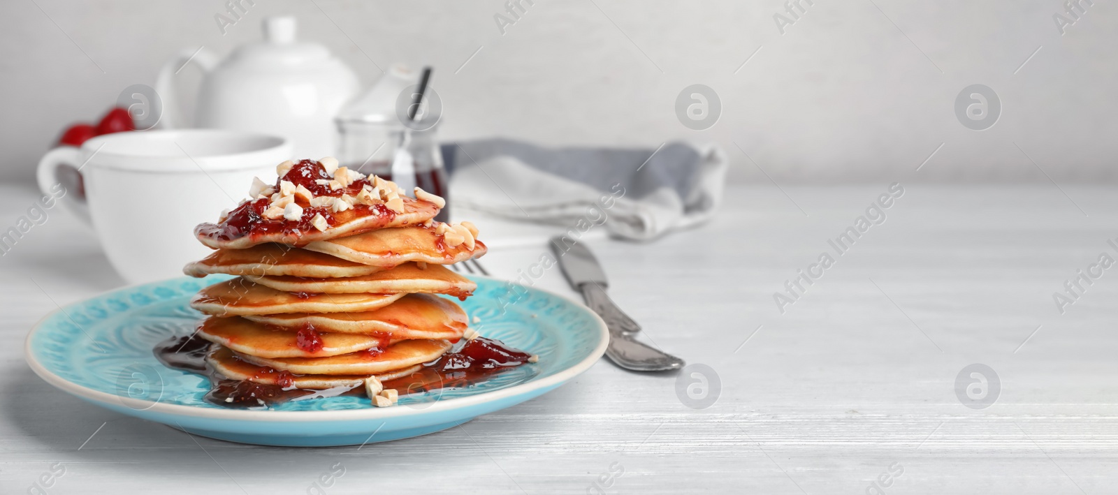 Image of Delicious pancakes with jam and nuts served for breakfast on table, space for text. Banner design