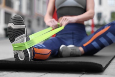 Photo of Woman doing exercise with fitness elastic band on mat outdoors, closeup