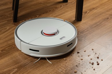 Robotic vacuum cleaner removing dirt from wooden floor indoors
