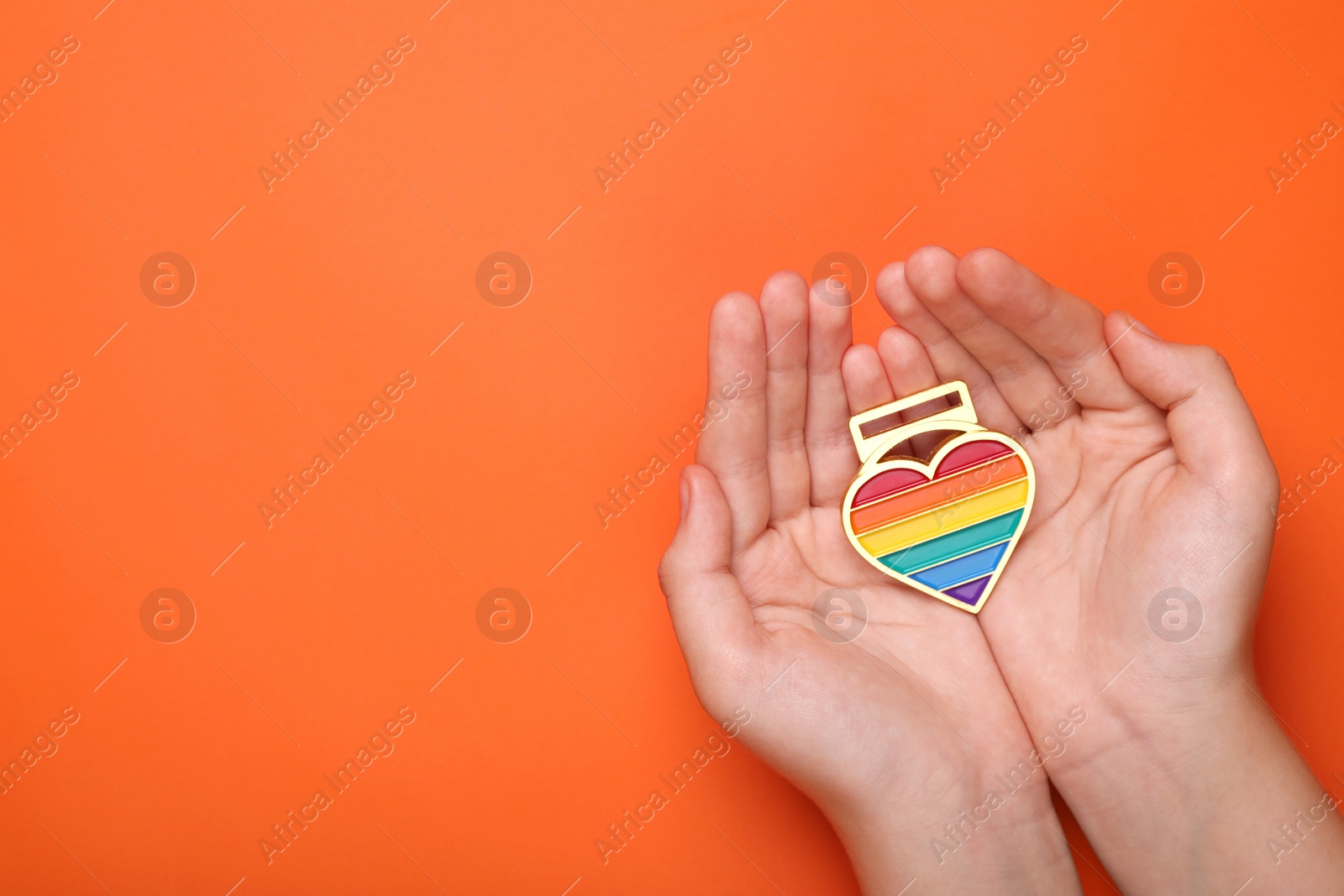 Photo of Woman with rainbow heart shaped pendant on orange background, top view and space for text. LGBT pride