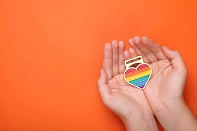 Woman with rainbow heart shaped pendant on orange background, top view and space for text. LGBT pride