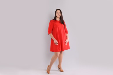 Beautiful overweight woman in red dress on light grey background