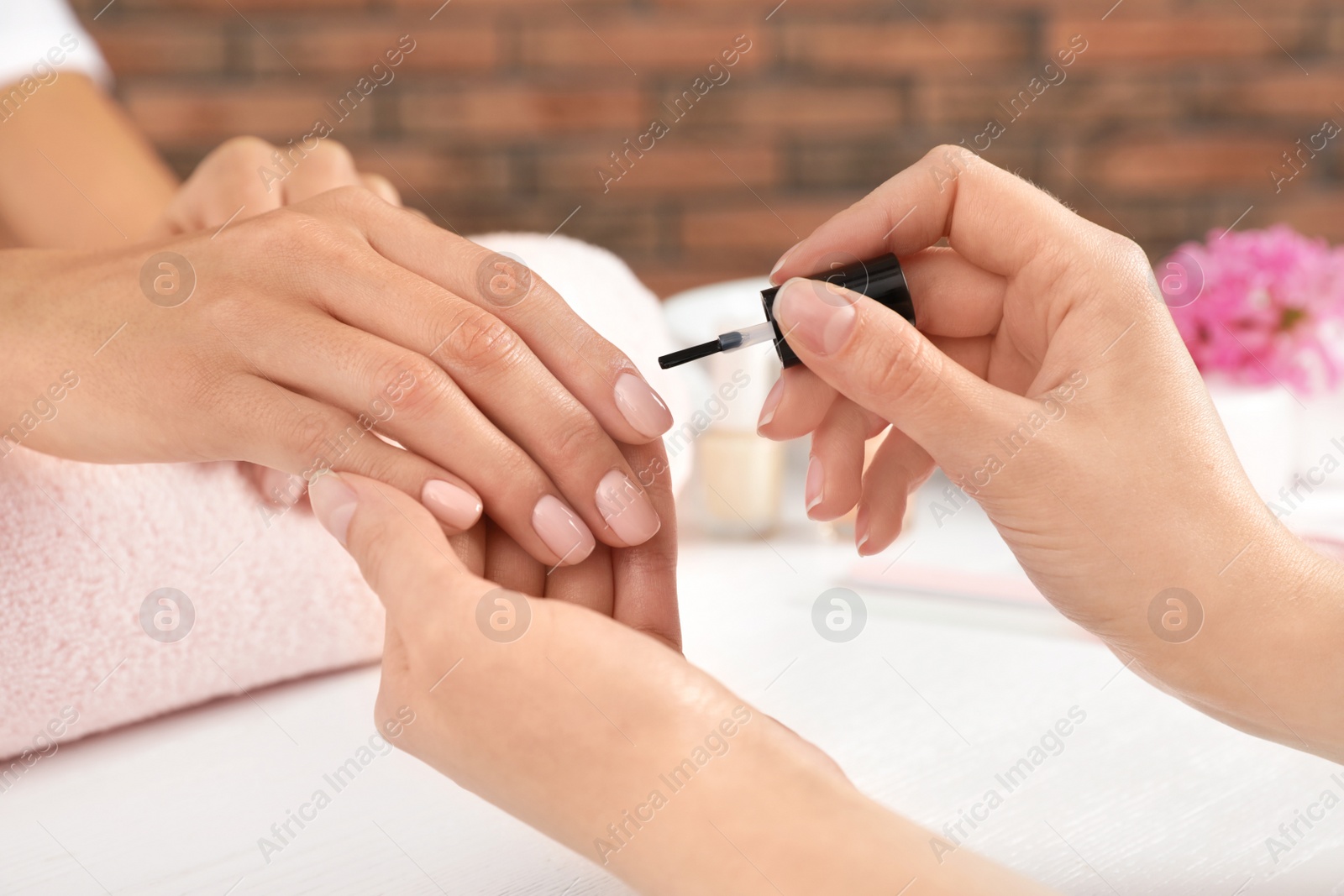 Photo of Manicurist applying polish on client's nails at table, closeup. Spa treatment