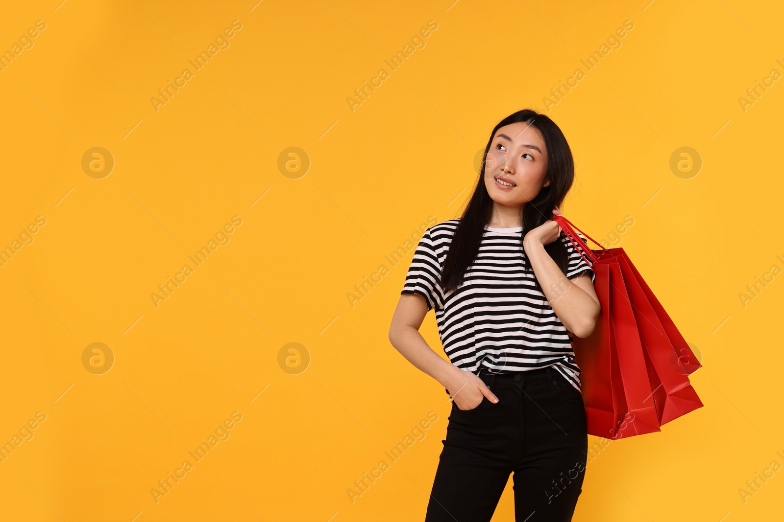 Photo of Smiling woman with shopping bags on yellow background. Space for text