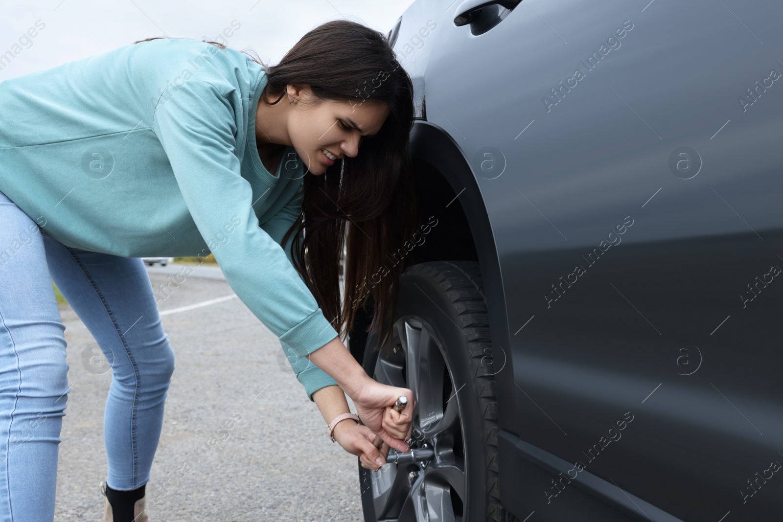 Photo of Young woman changing tire of car outdoors