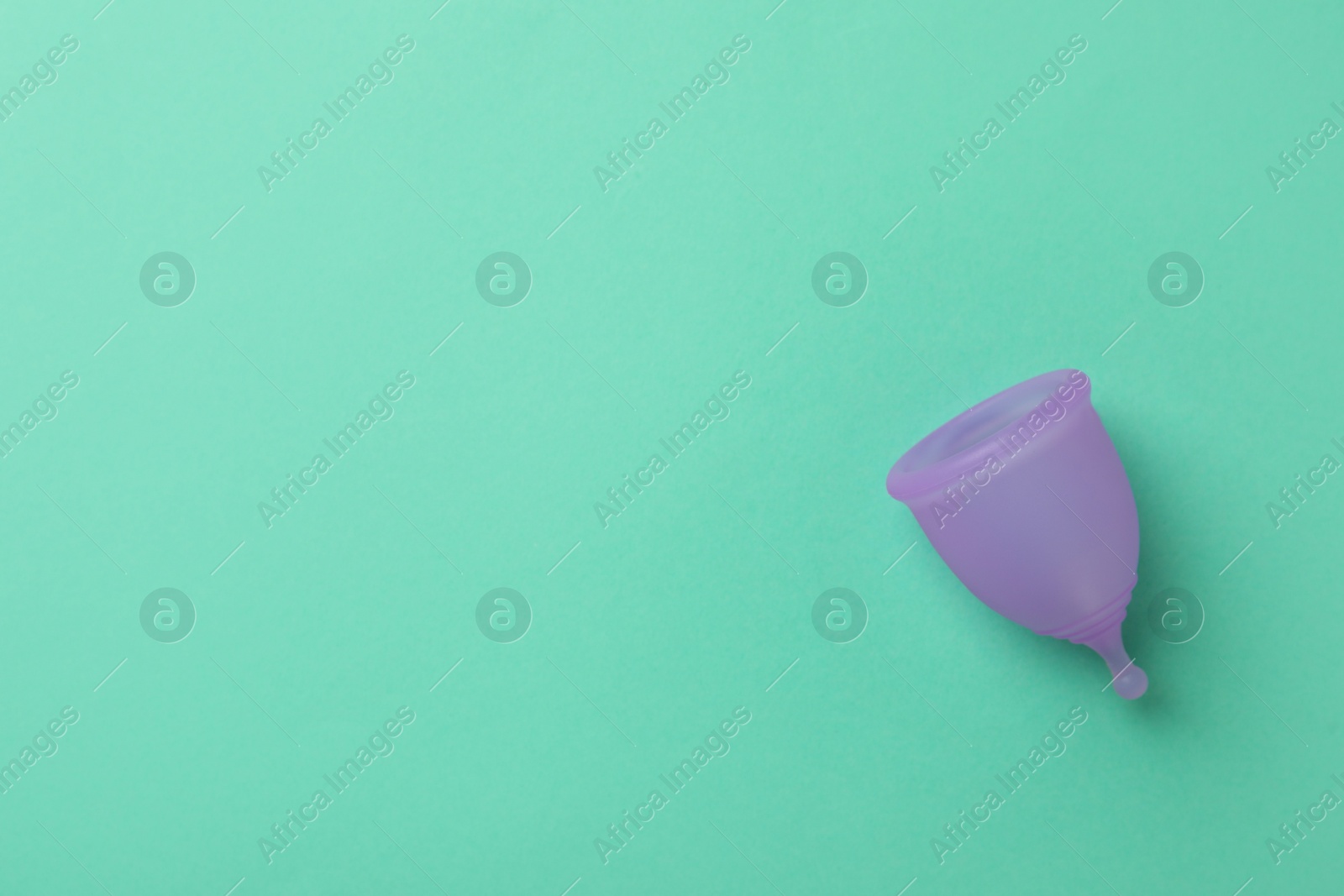 Photo of Menstrual cup on turquoise background, top view. Space for text