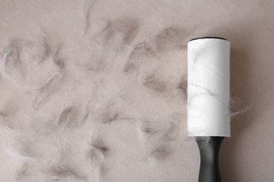 Photo of Modern lint roller and cat hair on light fabric, flat lay