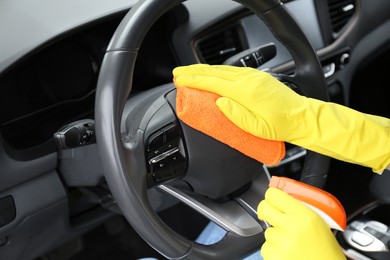 Photo of Woman cleaning steering wheel with rag in car, closeup