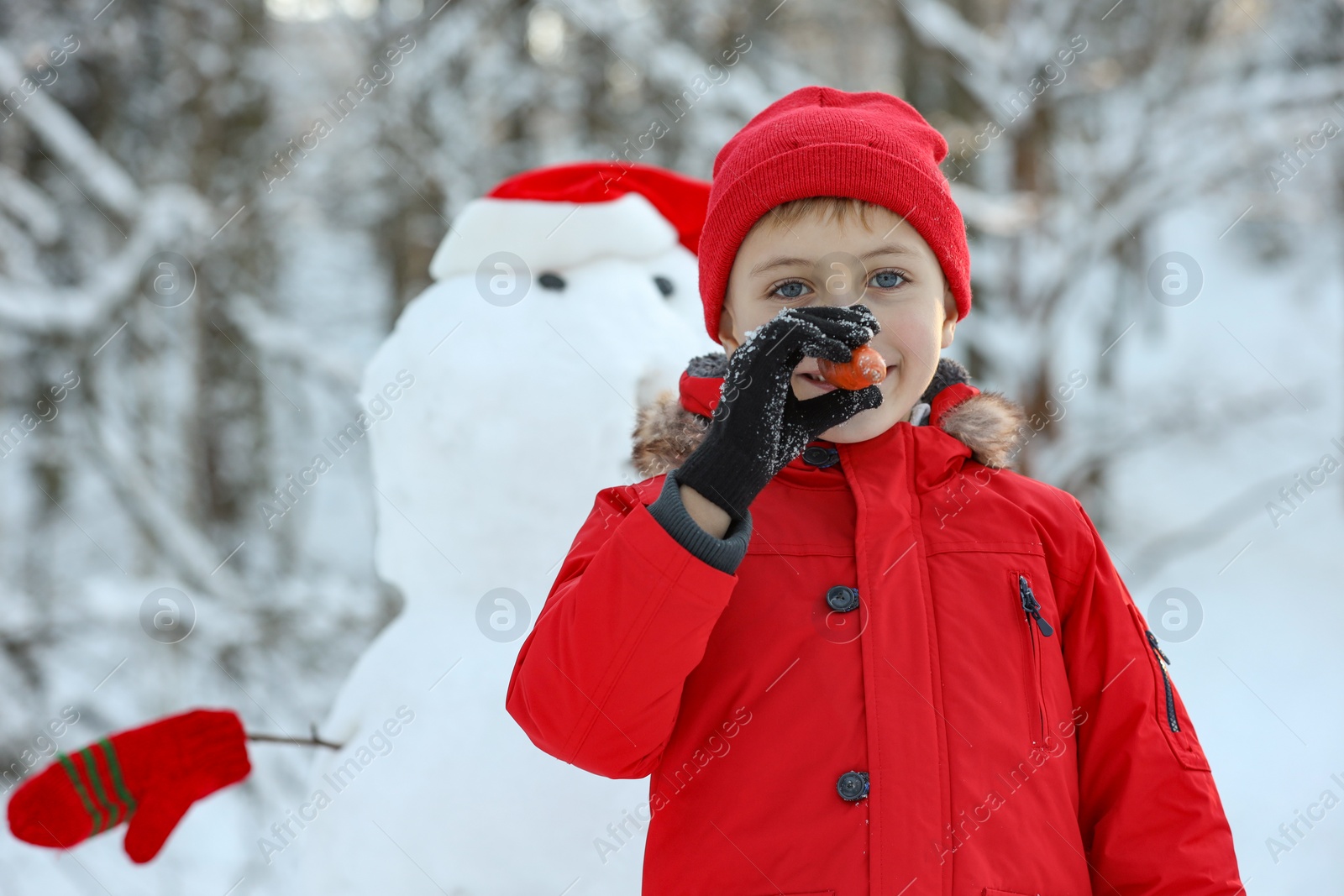 Photo of Cute little boy with carrot and snowman in winter park