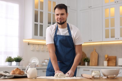 Photo of Making bread. Man kneading dough at wooden table in kitchen