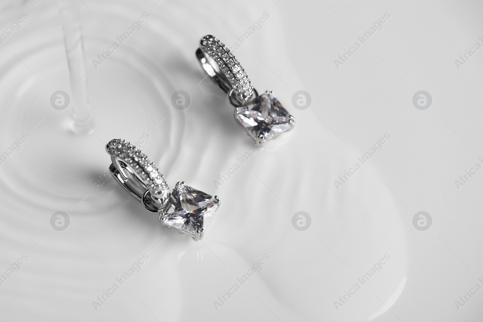 Photo of Luxury jewelry. Elegant earrings in flowing water on white background, space for text