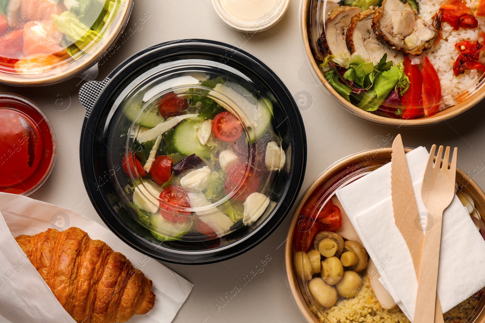 Photo of Tasty food in containers with wooden knife and fork on light grey table, flat lay