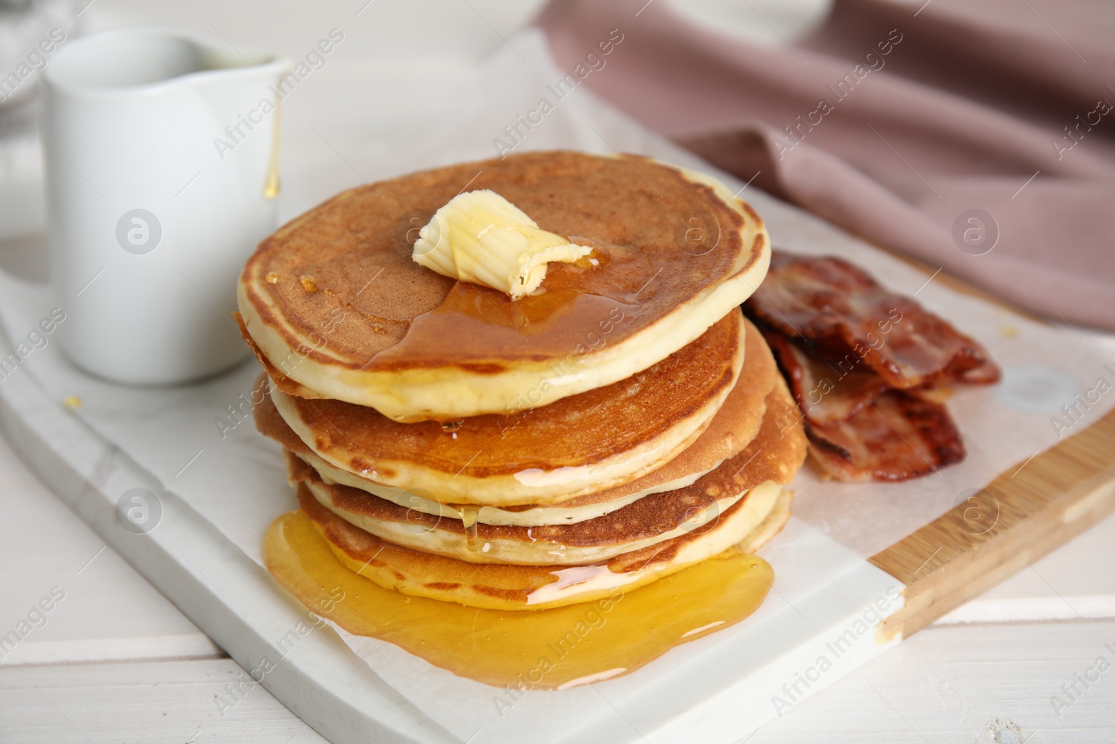 Photo of Delicious pancakes with maple syrup, butter and fried bacon on white wooden table, closeup