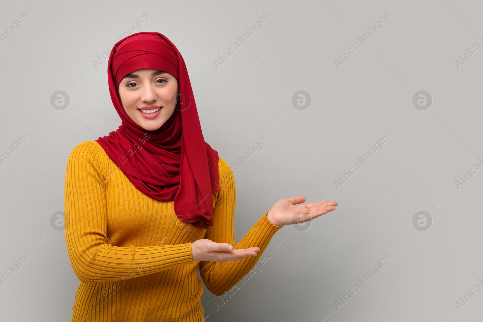 Photo of Muslim woman in hijab pointing at something on light gray background, space for text