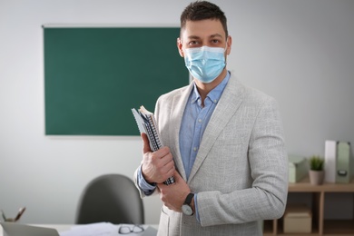 Photo of Teacher with protective mask and copybooks in classroom. Reopening after Covid-19 quarantine
