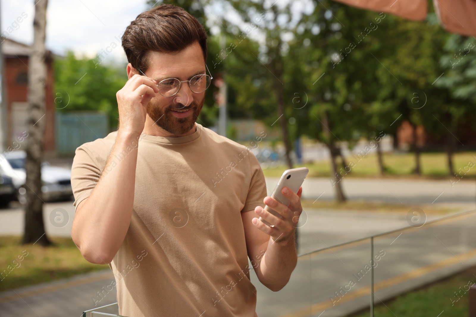 Photo of Smiling handsome bearded man with smartphone outdoors. Space for text