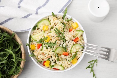 Cooked bulgur with vegetables in bowl on white wooden table, top view