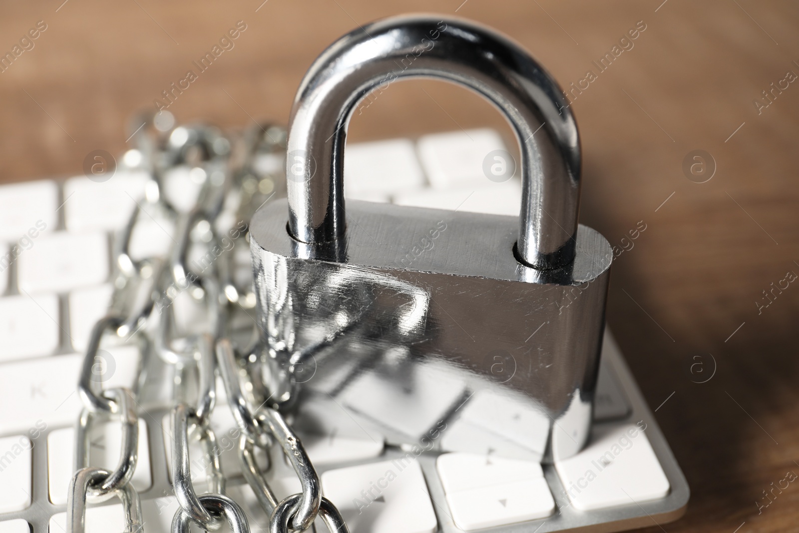 Photo of Cyber security. Keyboard with padlock and chain on wooden table, closeup